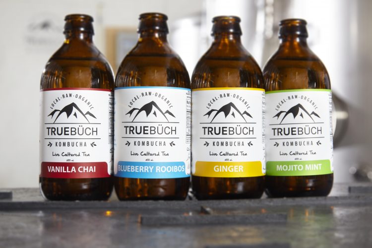 Four bottles of True Buch Kombucha are lined up. Flavours from left to right: vanilla chai, blueberry rooibos, ginger, mojito mint