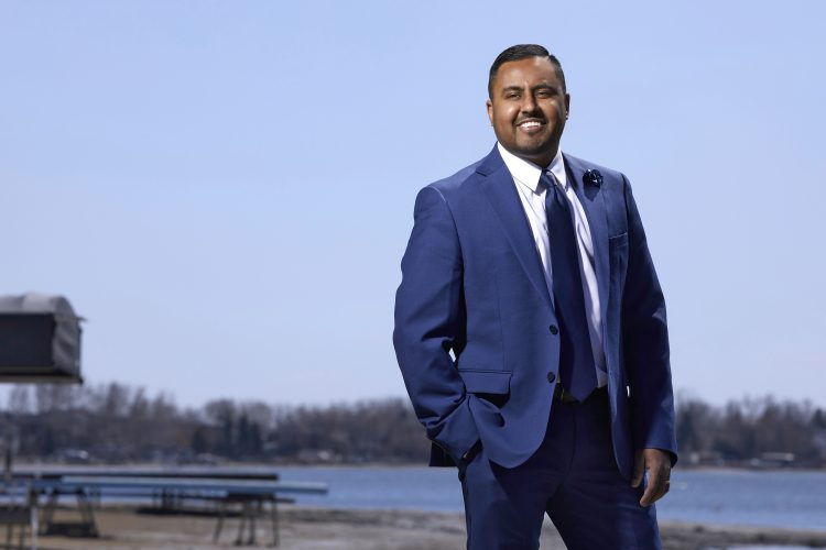 Isaac Achal CPA, CA poses with his hand in his pockets in front of a lake.