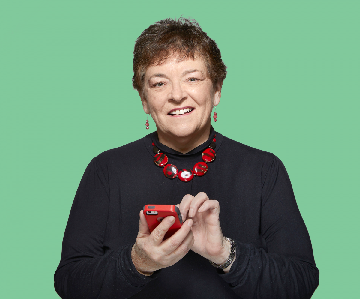 Betty Thompson FCPA, FCGA smiles at the camera while holding her phone.