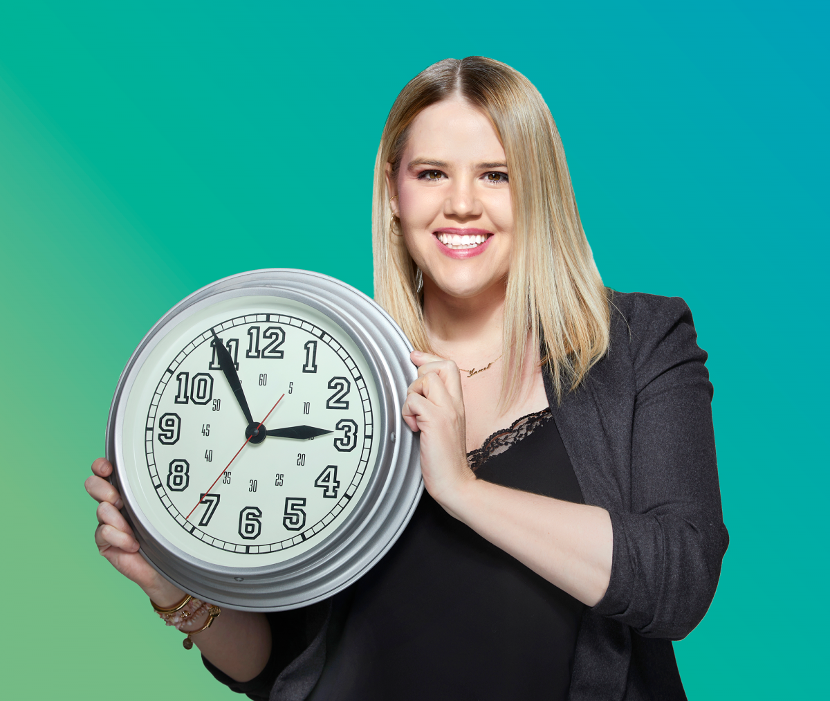 Janel Knispel smiles at the camera while holding a large clock.