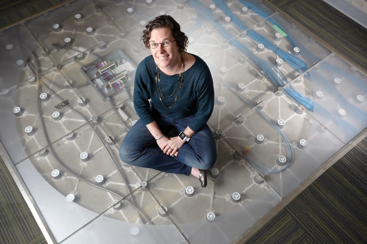 Melanie Laidlaw CPA, CGA sits on a floor designed to look like circuits and smiles up at the camera.