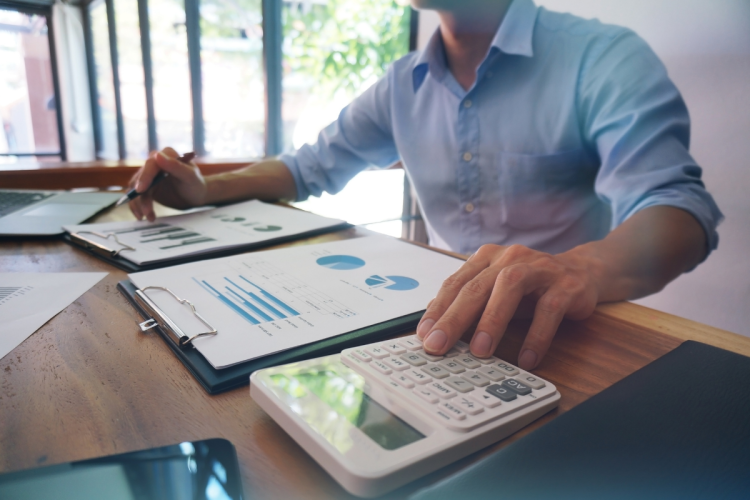 A person is sitting at a desk with printed graphs and a calculator in front of them.
