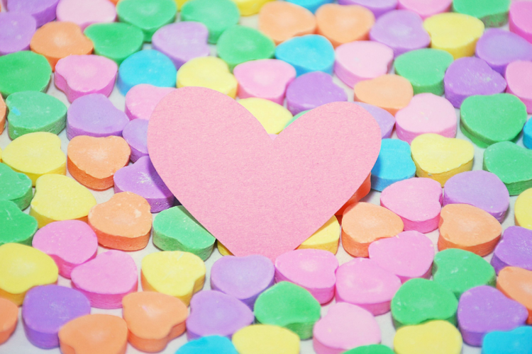 Conversation hearts in a variety of colours with a pink paper heart resting on top.