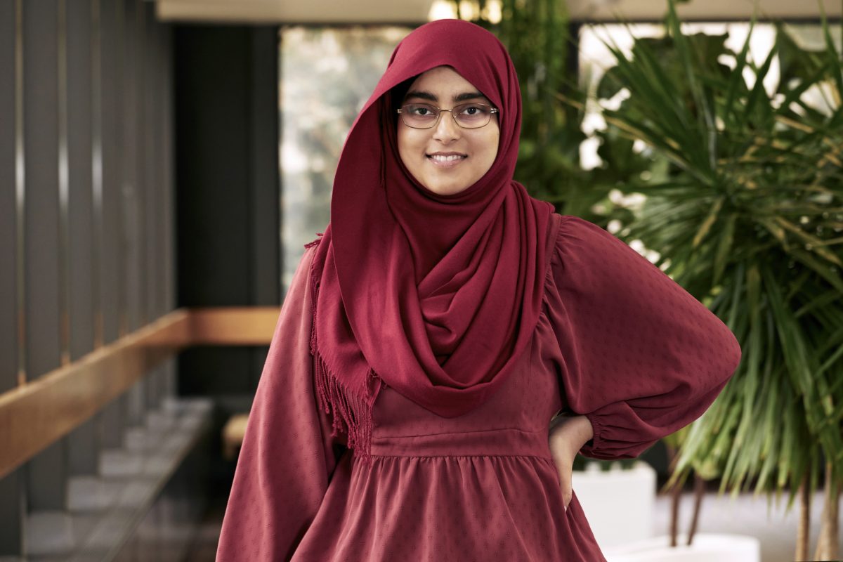 Izza Athar is smiling at the camera with one hand on her hip.