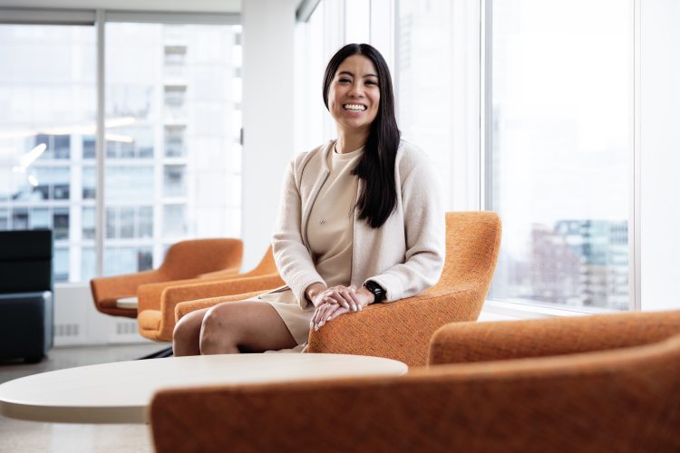 Julia Cruz CPA is smiling at the camera and sitting in an orange armchair. She is wearing a cream-coloured dress and blazer and has her hands crossed in front of her.