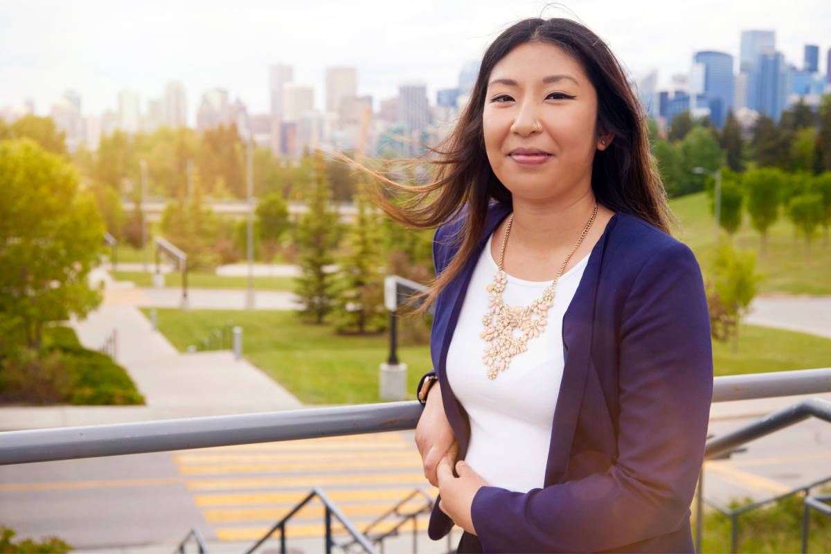 Arielle Valencia leans against a railing at the top of concrete stairs. She's wearing a blue blazer and smiling at the camera.
