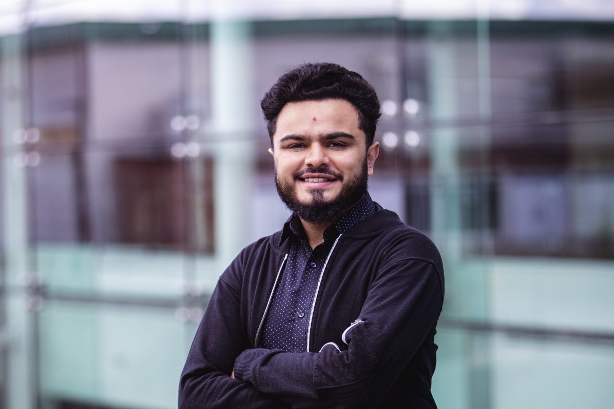 Vishal Vekaria leans against a glass wall with his arms crossed. He smiles into the camera.
