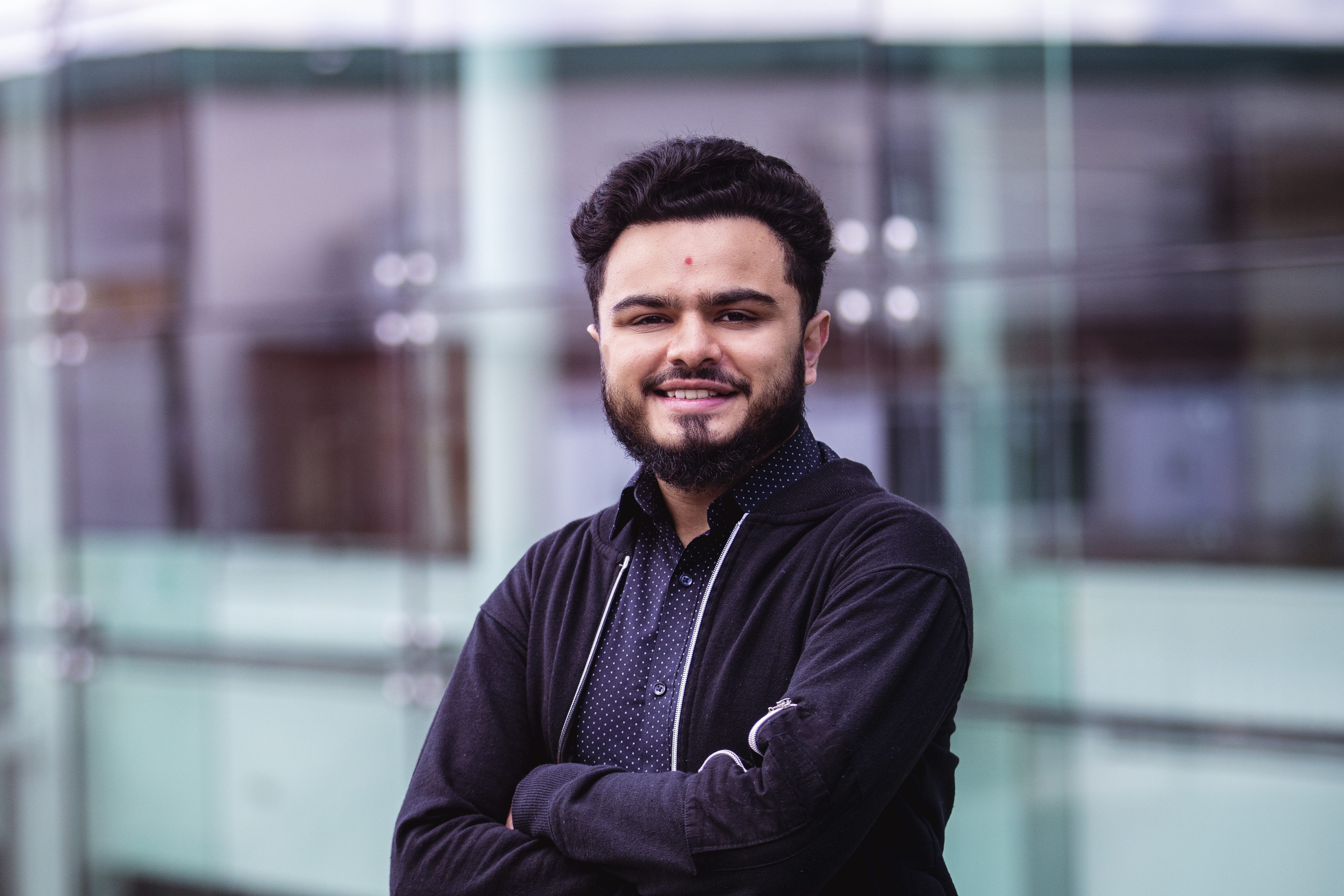 Vishal Vekaria leans against a glass wall with his arms crossed. He smiles into the camera.