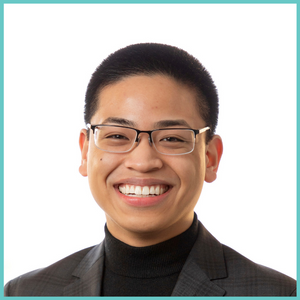 Red Enorme smiles at the camera. He is wearing a grey blazer, black turtleneck, and glasses.