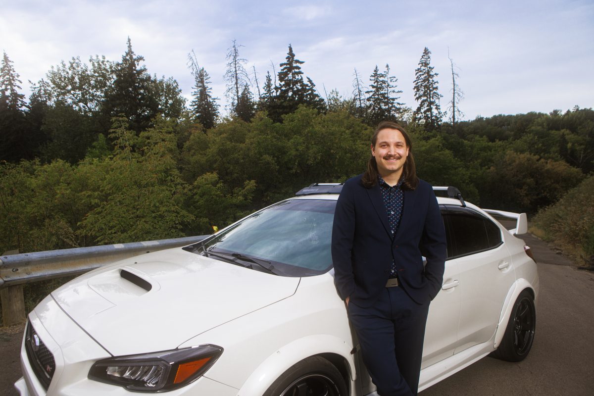 Roy Twinn CPA smiles at the camera while leaning against a white car with his hands in his pockets.