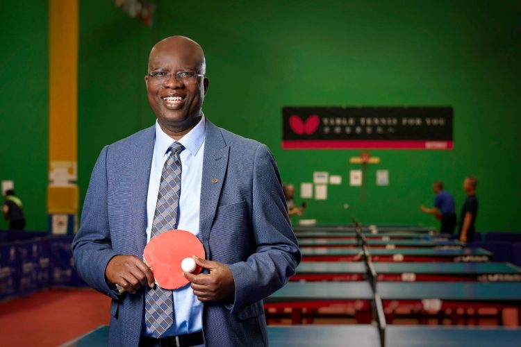 Kola Oladimeji CPA, CGA is smiling at the camera while posing with a ping-pong ball and paddle.