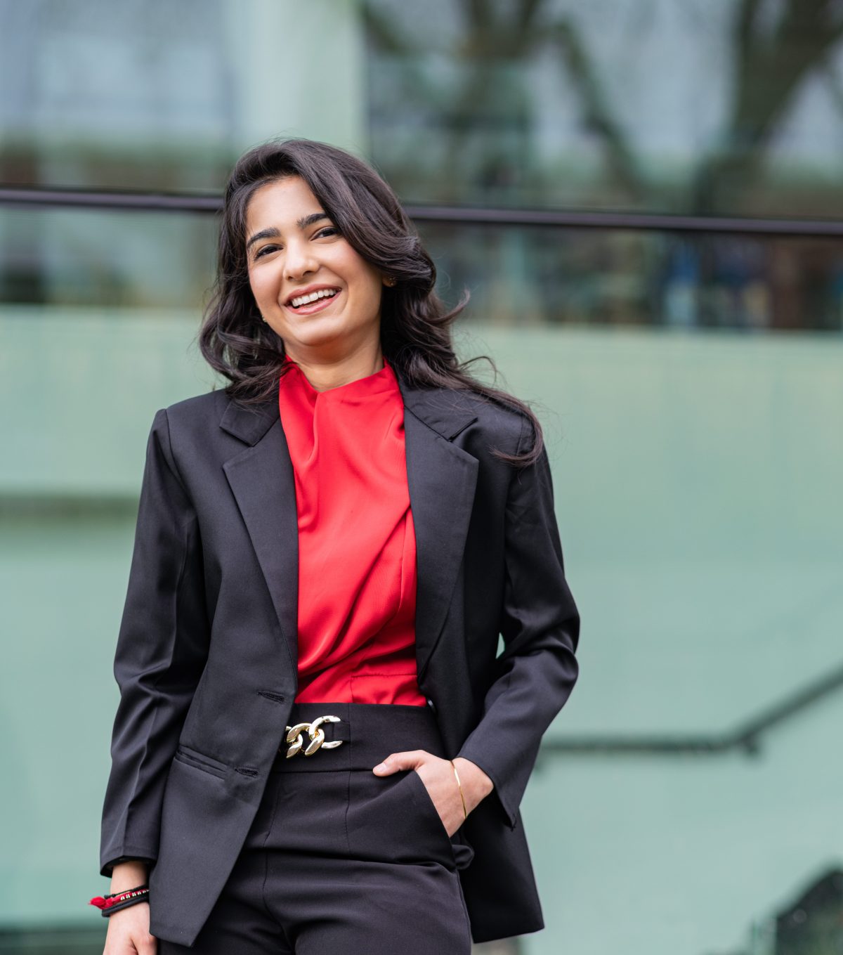 Diyal Duggal smiles at the camera with one in her pocket. She is wearing mostly black with a red blouse.