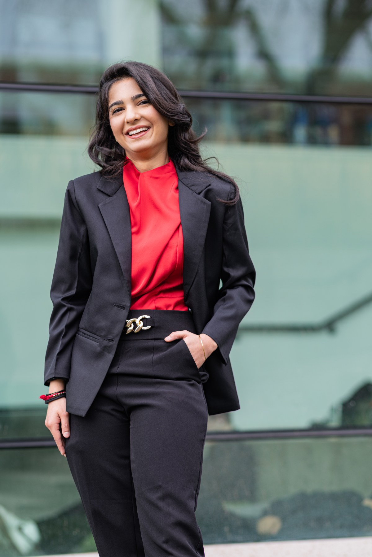 Diyal Duggal smiles at the camera with one in her pocket. She is wearing mostly black with a red blouse.